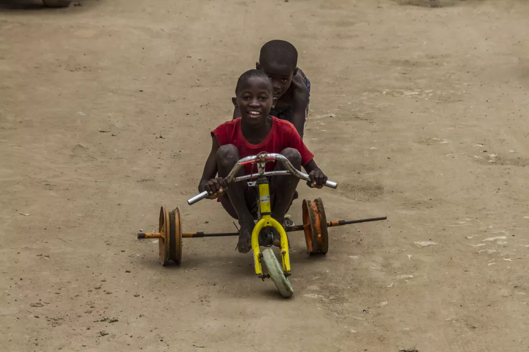 A boy pushes his friend in a tricycle made of reused parts