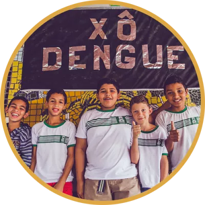 Foto mostra um grupo de meninos em frente a uma painel escrito xô, dengue