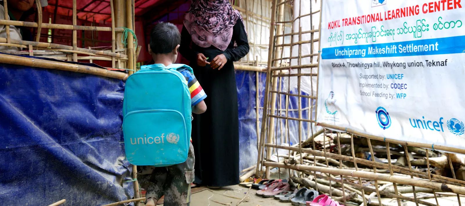Um menino rohingya chega para aulas em um centro de aprendizado estabelecido pelo UNICEF em um campo de refugiados. Ele tem uma mochila com o logotipo do UNICEF.