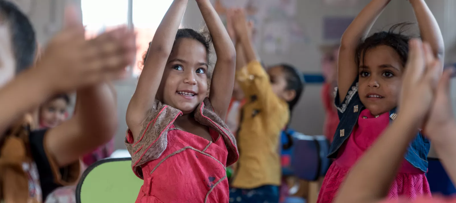 A child claps her hands above her head in a Kindergarten in Za'atari Refugee Camp
