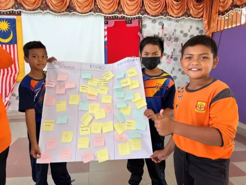 Three children show a poster they created with a disaster mitigation plan