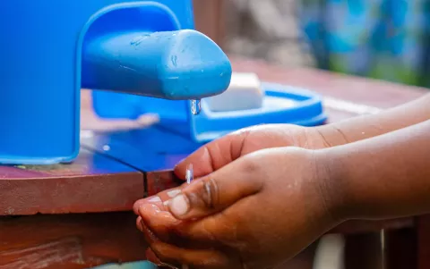 Water dripping in a child's hands from a blue plastic tap.