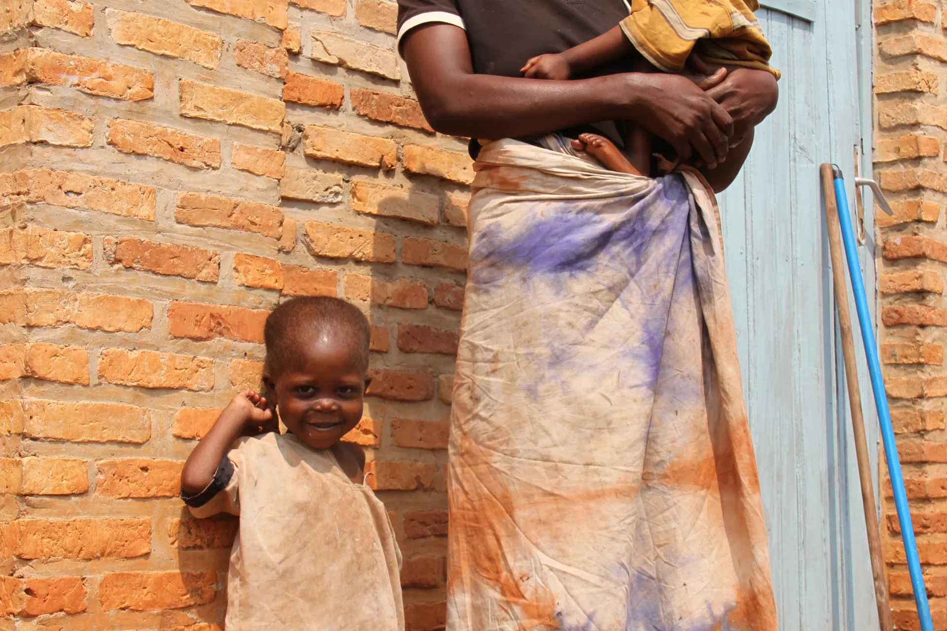 A woman holds her child in front of a brick wall, Burundi