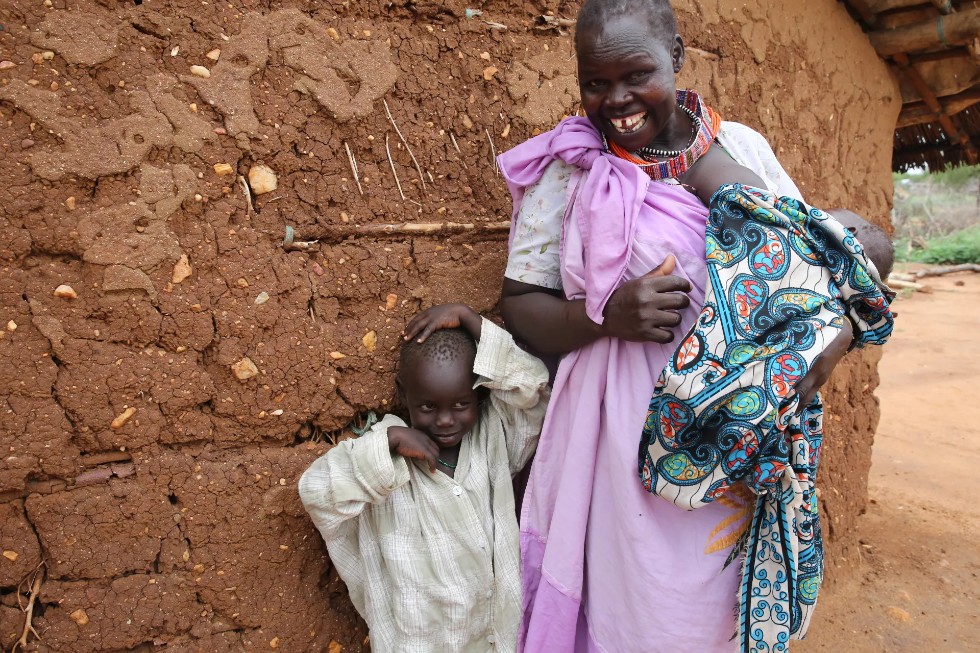 A mother stands with her son and new baby outside their home, South Sudan
