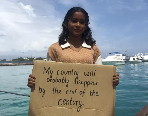A girl holding a sign that reads "My country will probably disappear by the end of the century".