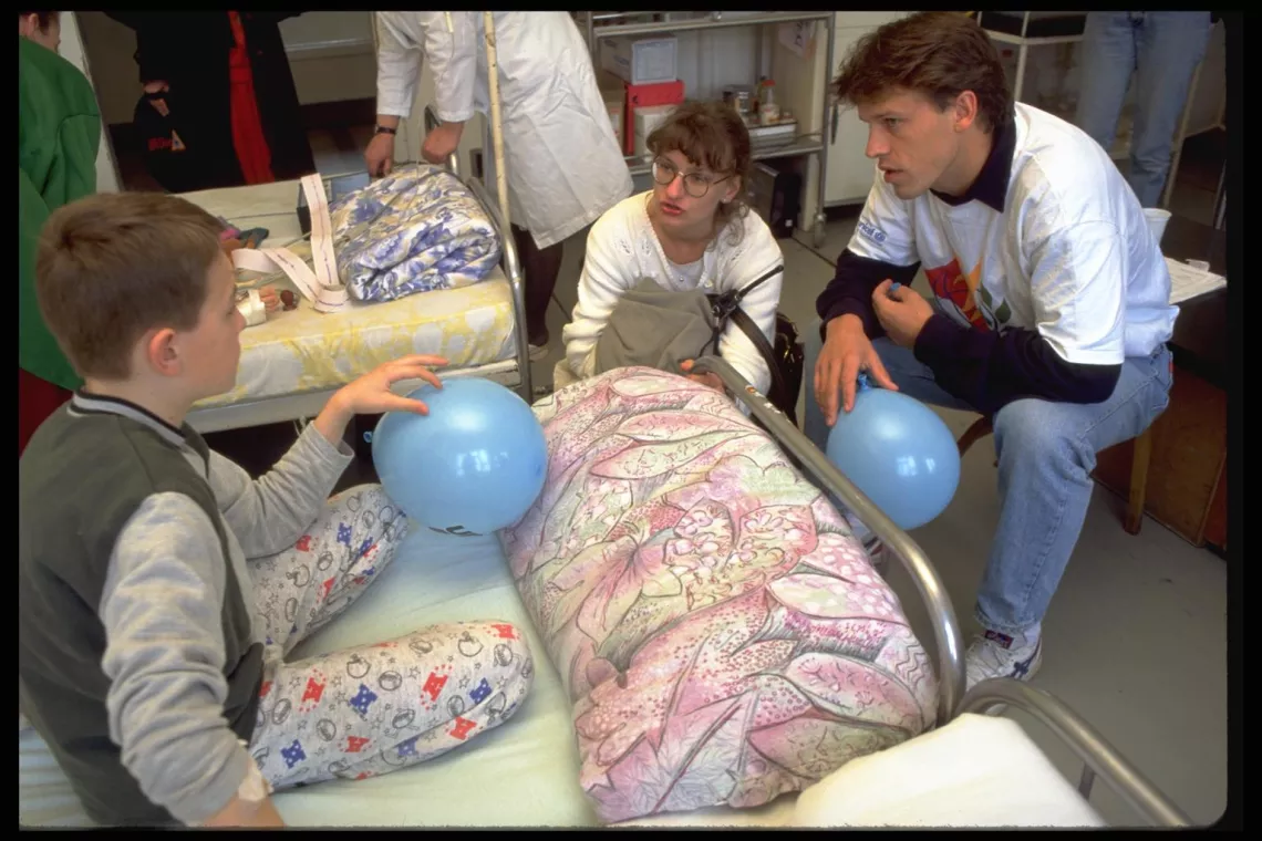 Accompanied by a UNICEF Sarajevo woman staffer (centre), UNICEF Special Representative for Sports Johann Koss (right) speaks to a boy patient, both holding UNICEF balloons Koss brought with him, at the UNICEF-assisted Kosevo Hospital in Sarajevo, Bosnia and Herzegovina. 