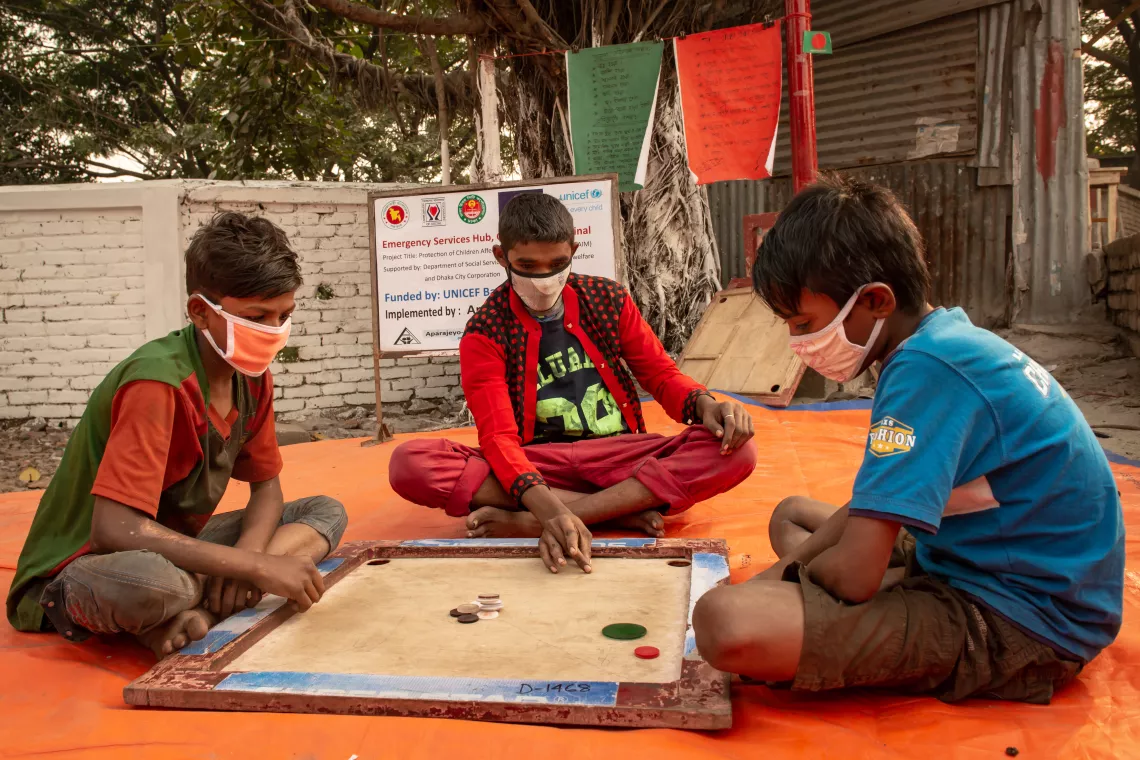 Young boys wearing masks are playing a game of carrom. 