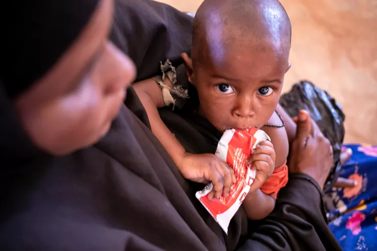 On 3 February 2022 in Somalia, a child feeds on a Ready-to-Use Therapeutic Food (RUTF) packet while his mother holds him waiting to receive assistance at Community Empowerment and Development Action Health Centre in Dolow.