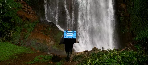 With a waterfall in the background, a porter carries UNICEF-provided vaccines on difficult terrains on the way to a vaccination campaign at the Barpak Village Development Committee (VDC) health post in Gorkha District, the epicentre of the earthquake in Nepal in 2015.