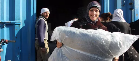 A smiling woman holds UNICEF blankets, among the five she just received during a distribution at a Syrian Arab Red Crescent warehouse, in the city of Lattakia, in December 2013.