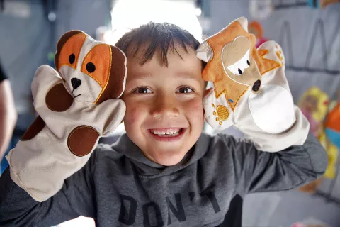 A little boy smiles with his hands covered by puppets.