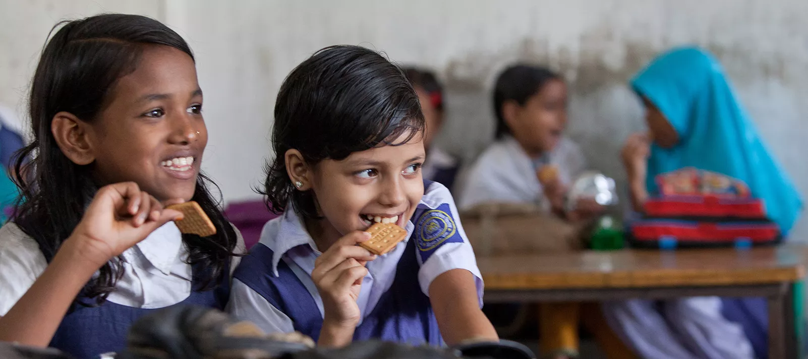 Two smiling schoolgirls of grade three enjoy protein-rich biscuits during their break period at Sher-E- Bangla Govenment Primary School, in Dhaka, Bangladesh, in October 2013.