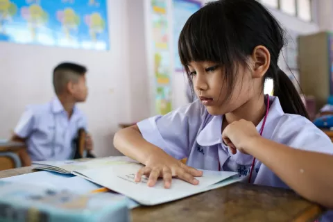 Inside a classroom, a girl in a student uniform is reading a book.