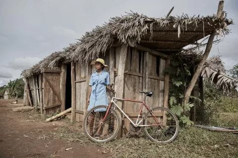 เด็กสาวในมาดากัสการ์กำลังยืนอยู่ข้างๆ จักรยาน หน้าห้องเรียนที่ถูกพายุไซโคลนทำให้เสียหาย