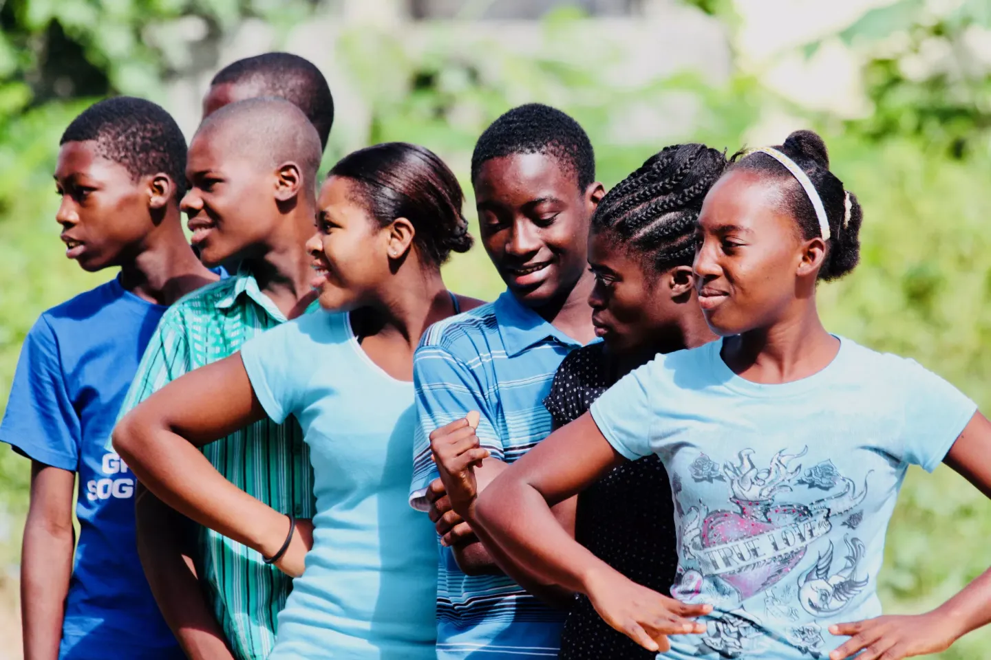A group of adolescents in a field in Haiti standing in a line with their elbows akimbo.