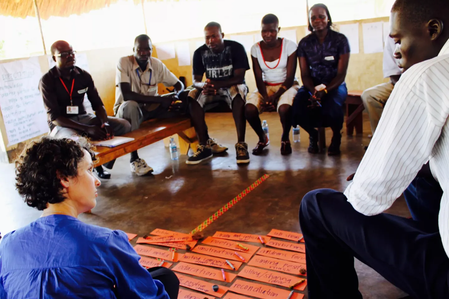 A group of young adults sit in a circle talking. On the floor between them are small pieces of paper with handwritten notes arranged in lines.