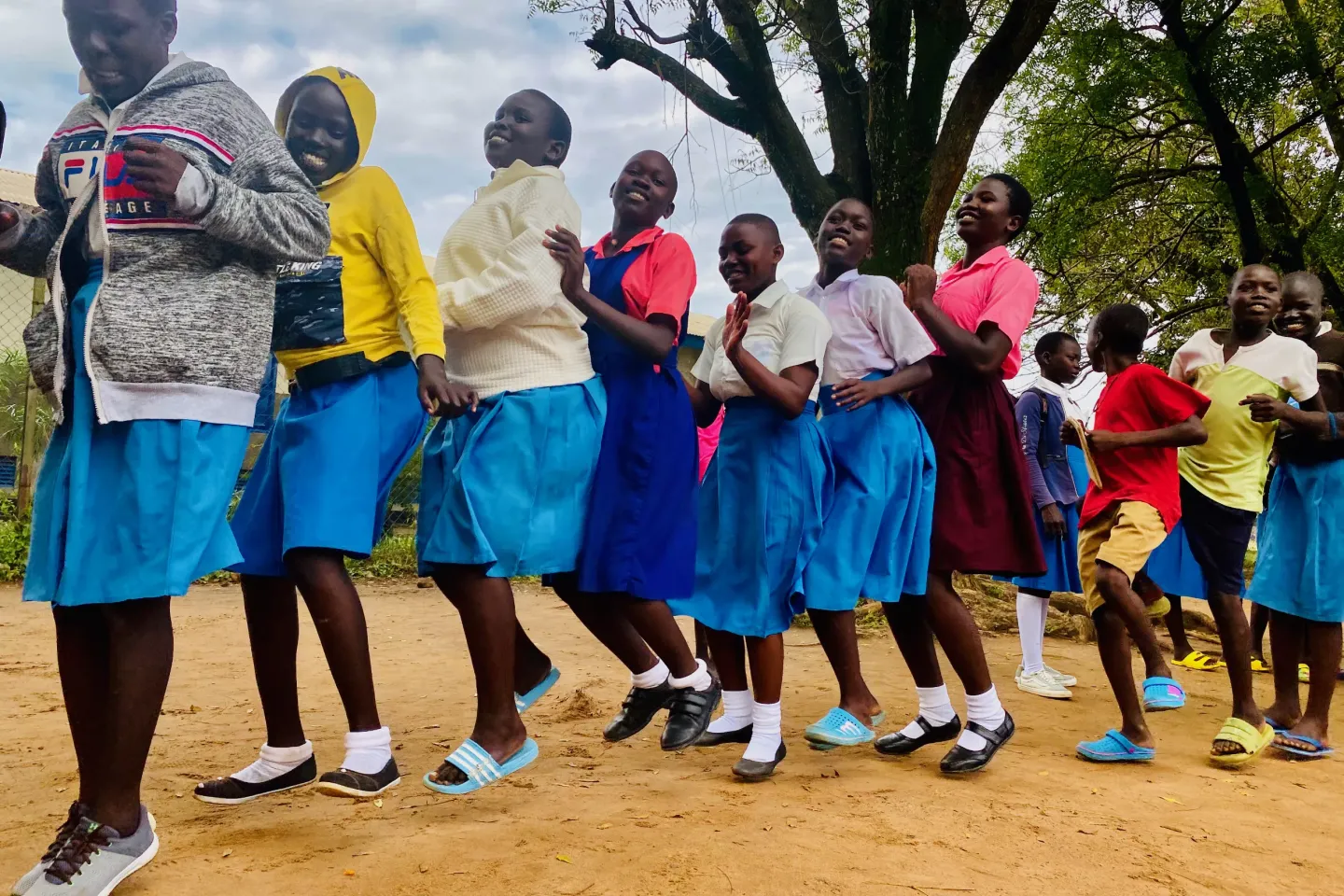Adolescent girls in Uganda wearing school uniforms standing in a line, jumping and smiling