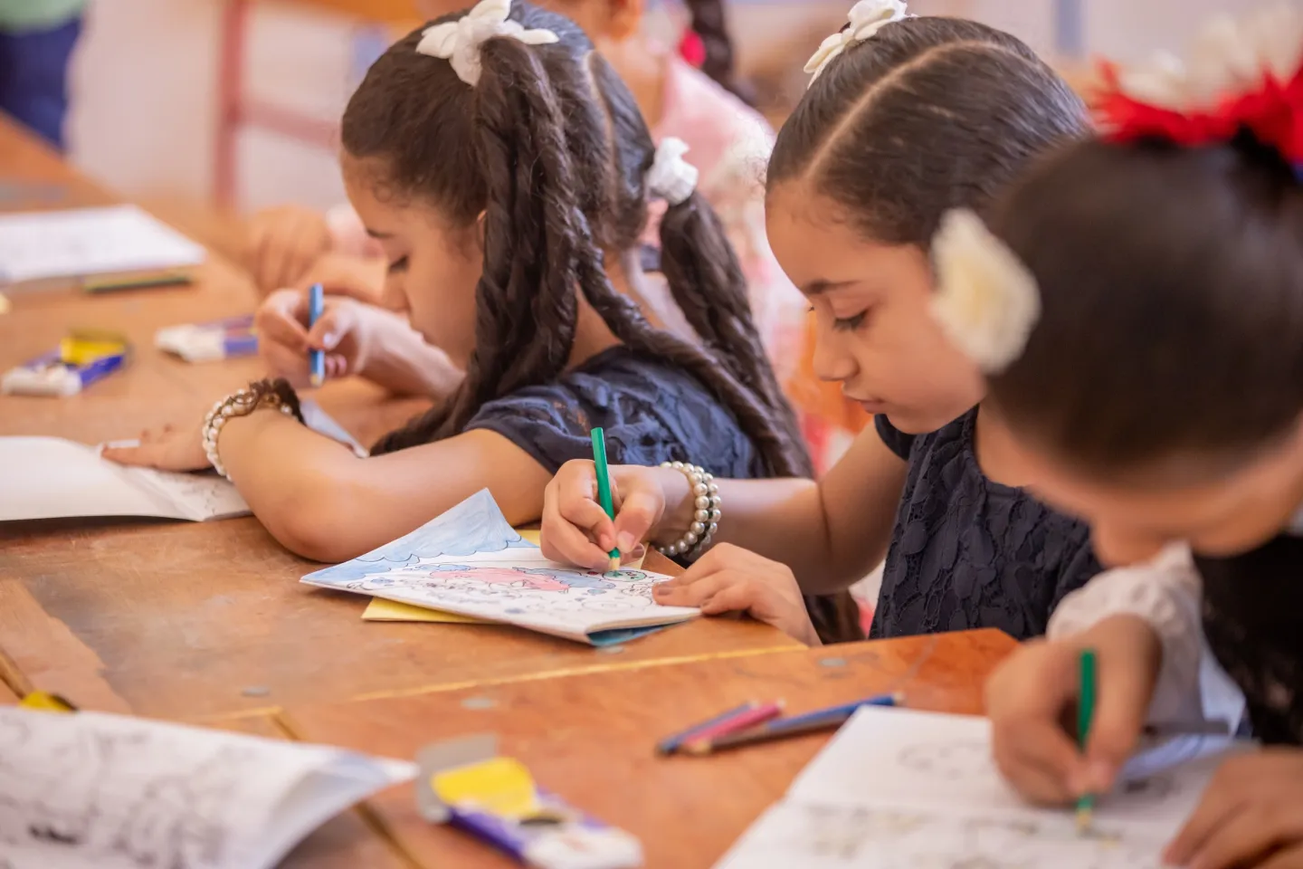 Girls sit at a desk drawing and writing.