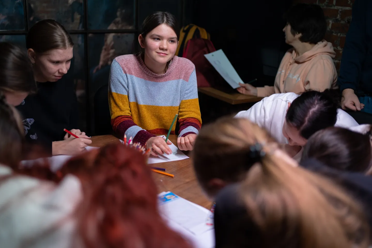 A group of young people sit around the table talking and drawing.