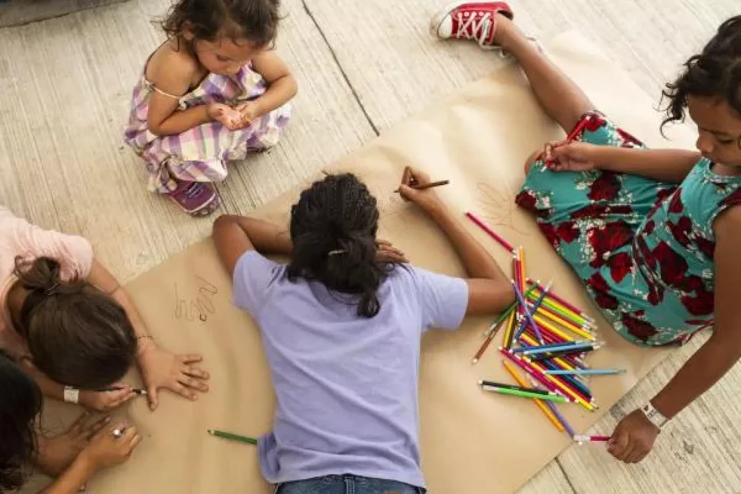 Four chidren are sitting or lying on a floor that is covered in large pieces of paper, drawing on the paper. They are viewed from above.