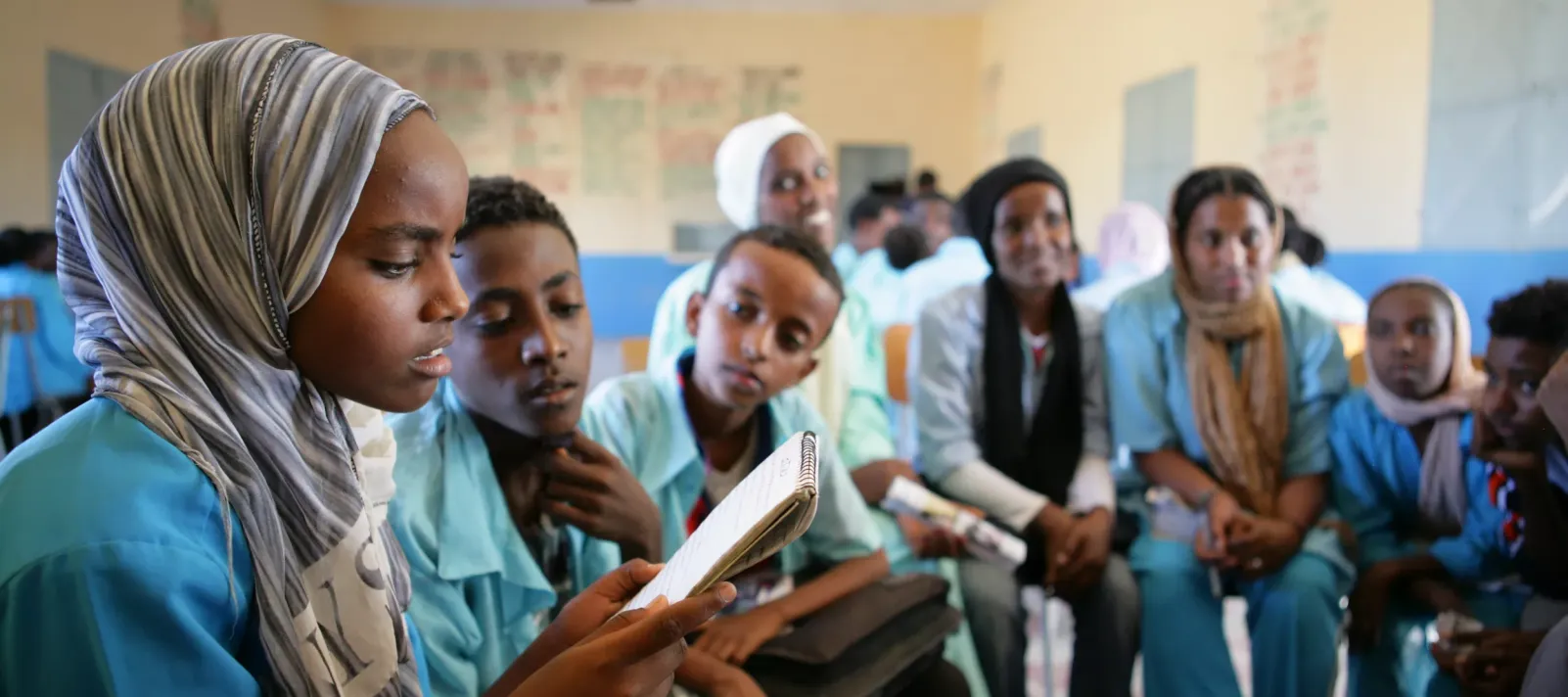 A group of youth sit in a circle while a girl reads out something