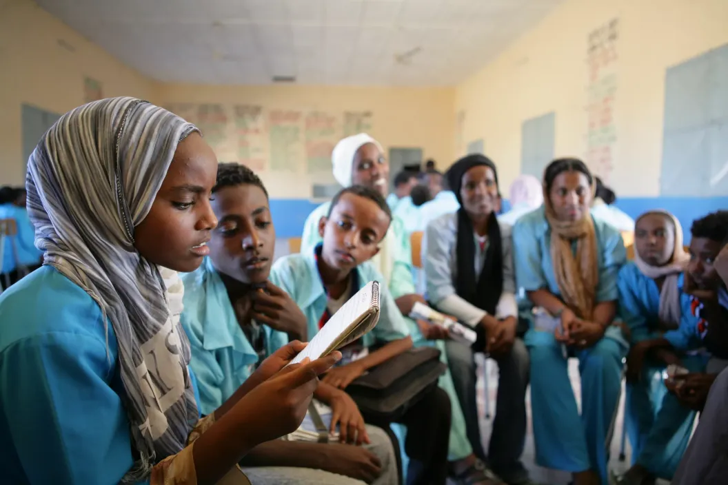 A group of youth sit in a circle while a girl reads out something