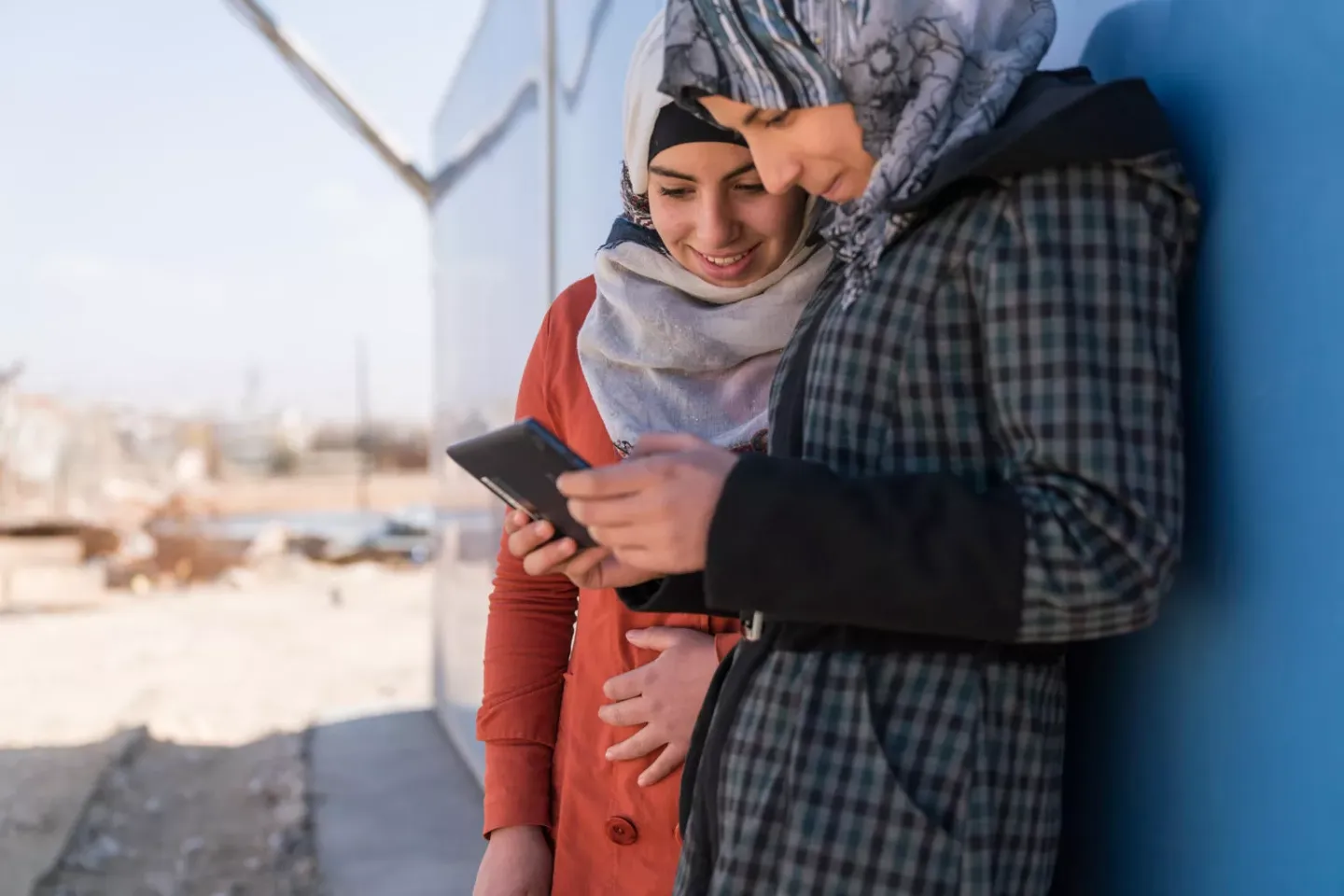 Two girls wearing hijabs lean close to eacho the looking at cellphone