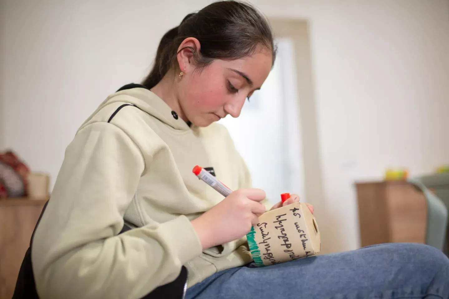 An adolescent girls wearing a tan sweater decorates as coffee mug