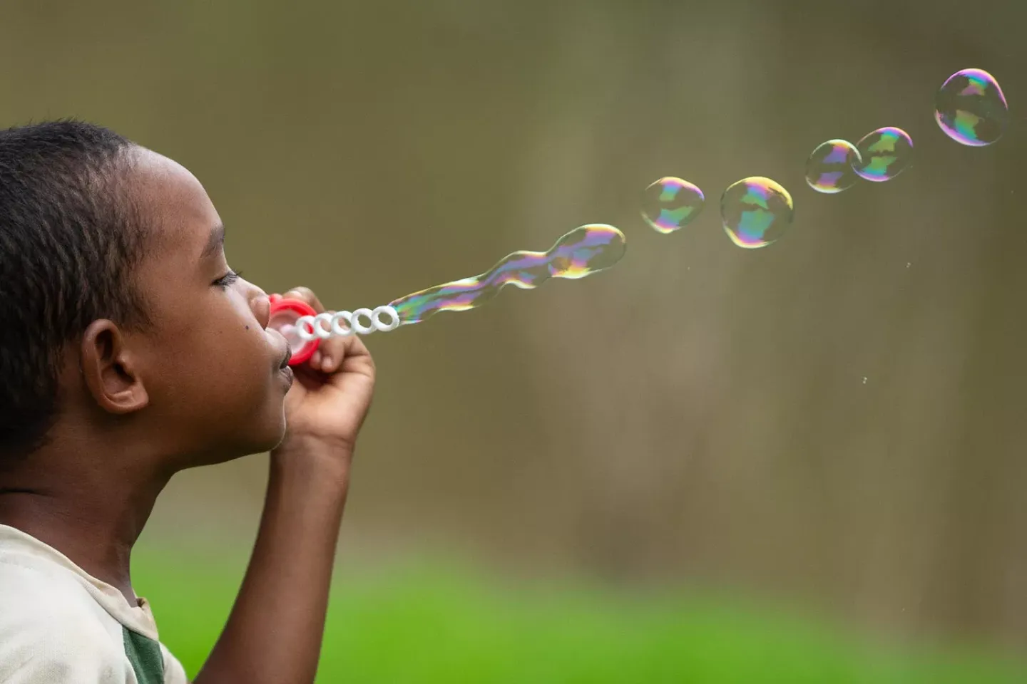 A young boy blows a long trail of soap bubbles, leading left to right across the image 