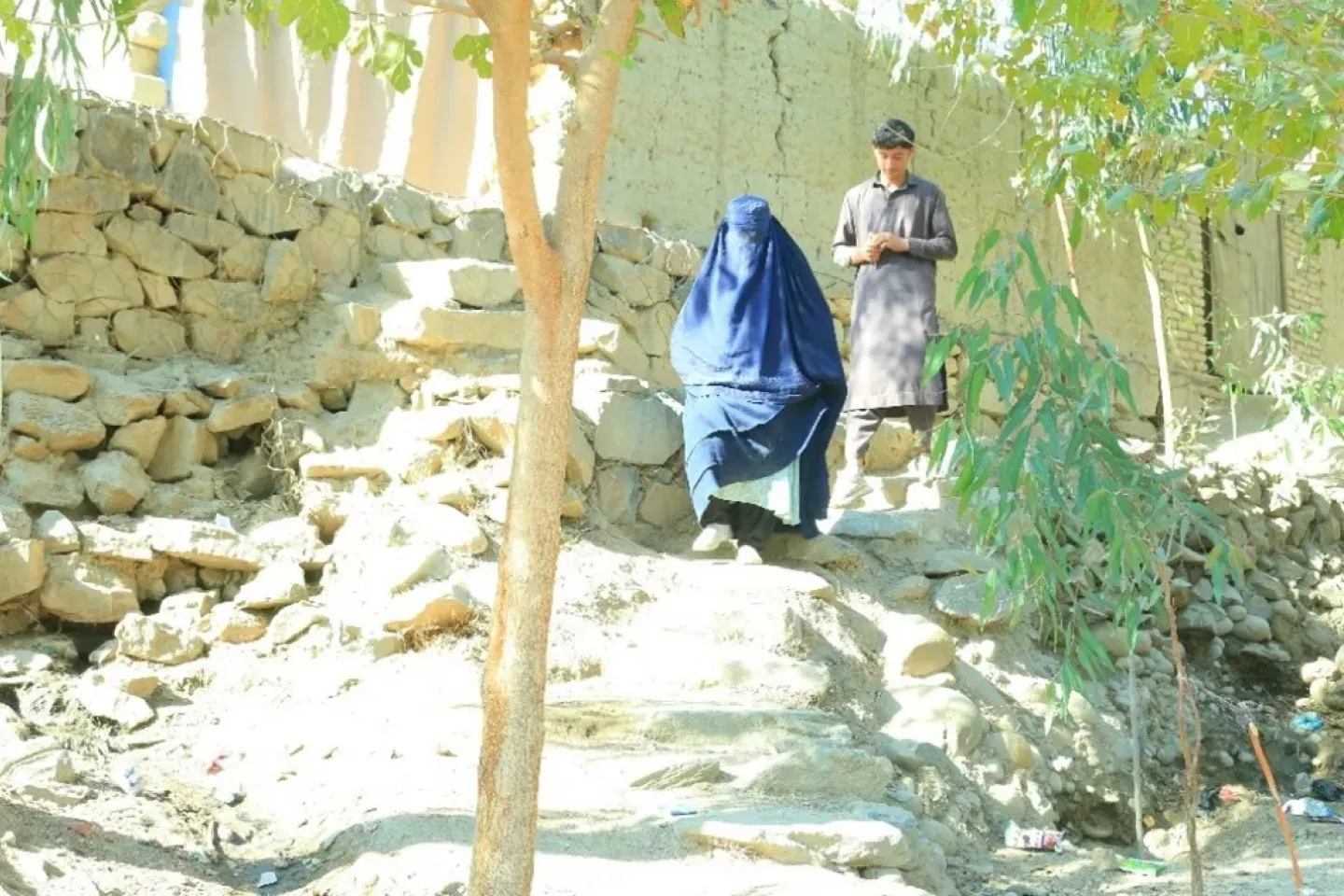 Sediqa (45) walks along a rocky path with her son, who serves as her mahram, as they move from one household to the next during the polio campaign in Laghman Province. 