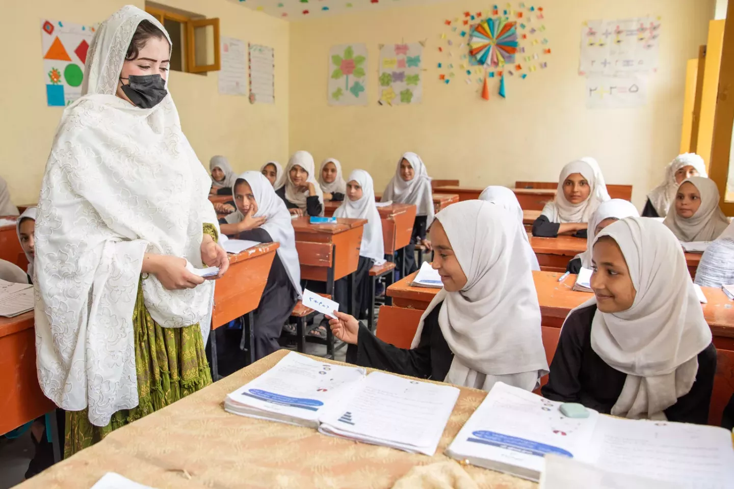 On 4th May 2025, Lima Azizi is teaching mathematics at grade third of Hazrat Abubekr-e-Sediq high school. Lima Azizi has been teaching for almost three years at Hazrat Abubekr -e- Sediq high school. She recently attended a UNICEF-supported training course for teachers. She is distributing small cards between her students to prepare them for a classroom activity. She says she learned about this activity in the training and found it to be a very useful and interesting method of teaching.