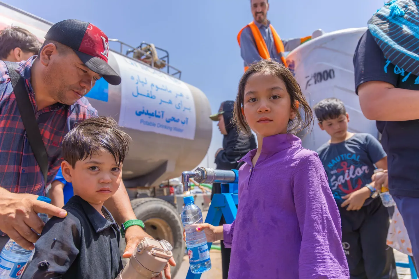 On 1 July, children collect safe drinking water from a tap at the Islam-Qala border reception centre in Herat Province. Due to the recent surge in returnees from Iran, access to clean water has become a critical concern. In response, UNICEF is delivering between 90,000 to 120,000 litres of potable water daily through emergency water trucking at the zero-point reception area.