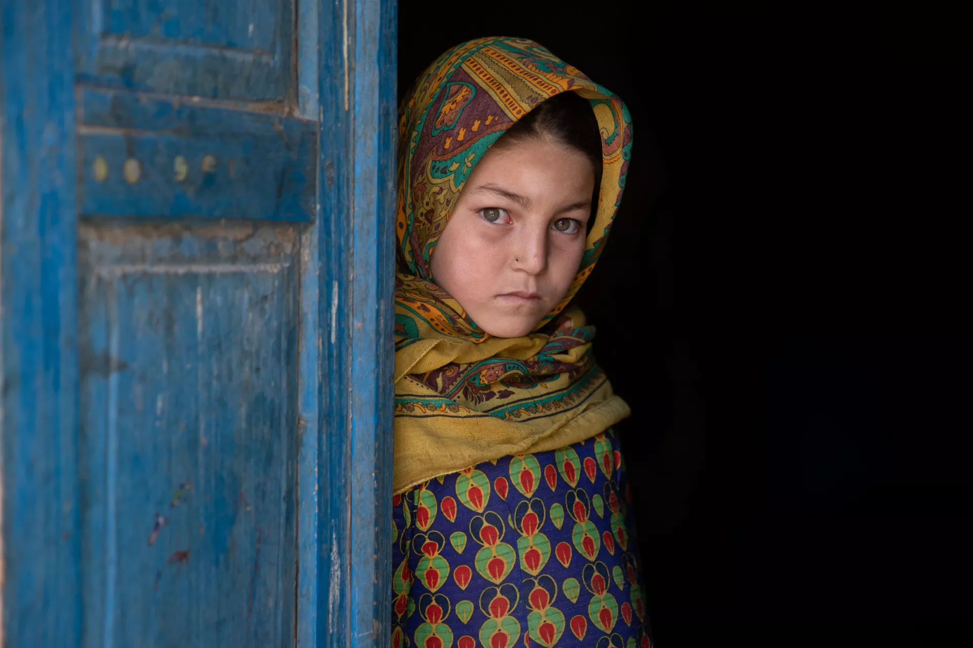 In October 2022, in Badghis Province, Afghanistan, 9-year-old girl Asna stands by the door of her home, where her family recently received cash assistance from UNICEF.