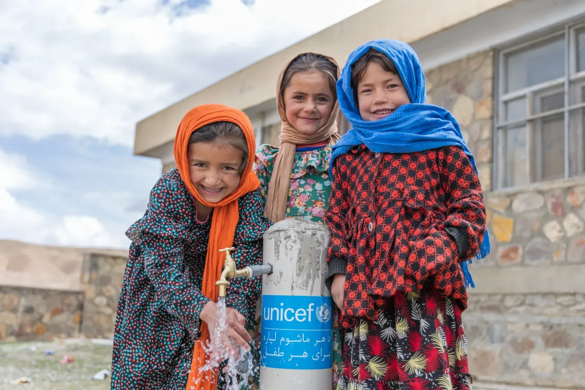 Farnoosh (centre) stands with her friends beside a water tap at Badgah School in Jonobe Badgah village, where access to safe water is helping students learn, play and thrive. 