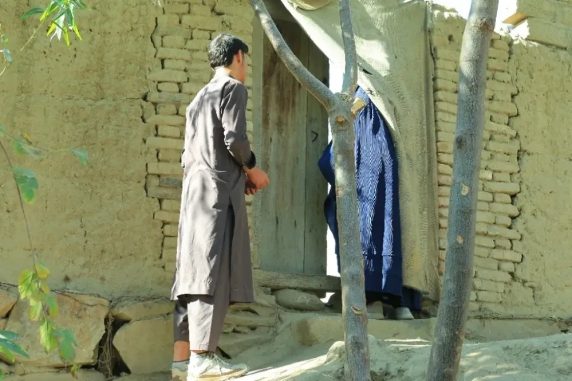 Sediqa (45), a social mobilizer for polio programme stands at the entrance of a home, listening and responding to questions from caregivers, while her son waits nearby during the visit