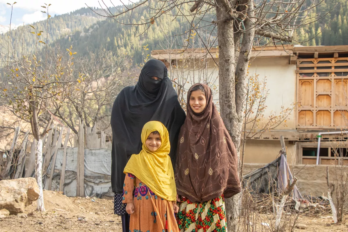 On 28 November 2023, Saeed Khanum stands with her two daughters, Farina, 5, and Farzana, 10, outside their home in Parun district, Nuristan province, Afghanistan, after just receiving cash assistance from UNICEF.