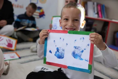 child showing his drawing of two hands smiling