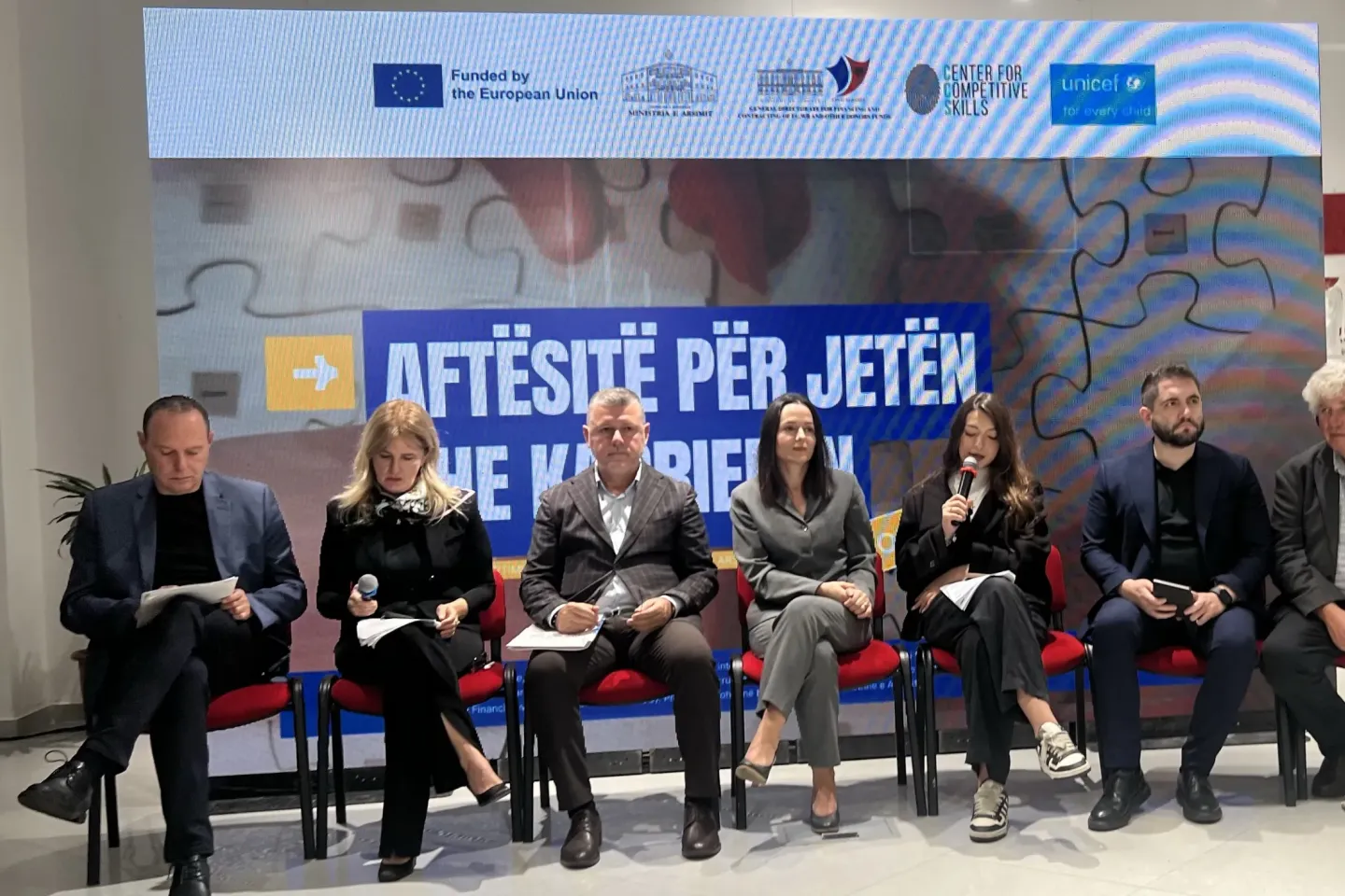 Panel discussion with seven speakers seated before a banner reading &ldquo;AFT&Euml;SI P&Euml;R JET&Euml;N&rdquo;.