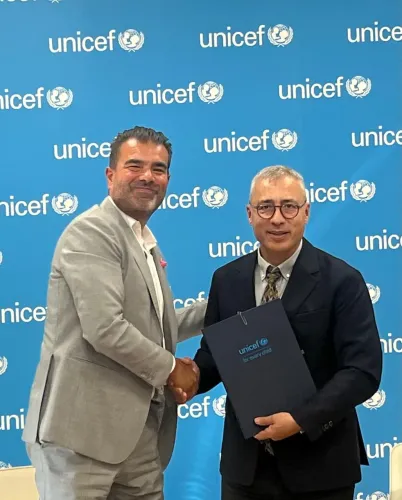 Two men shake hands in front of a UNICEF backdrop; one holds a folder, indicating a partnership agreement.