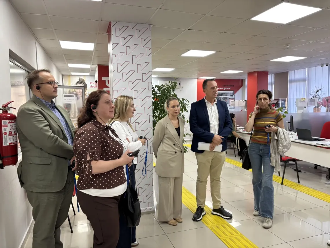Group listens to a speaker in a modern hallway with tactile yellow floor guides and signage.
