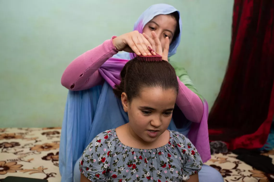A schoolgirl gets her hair brushed by her sister