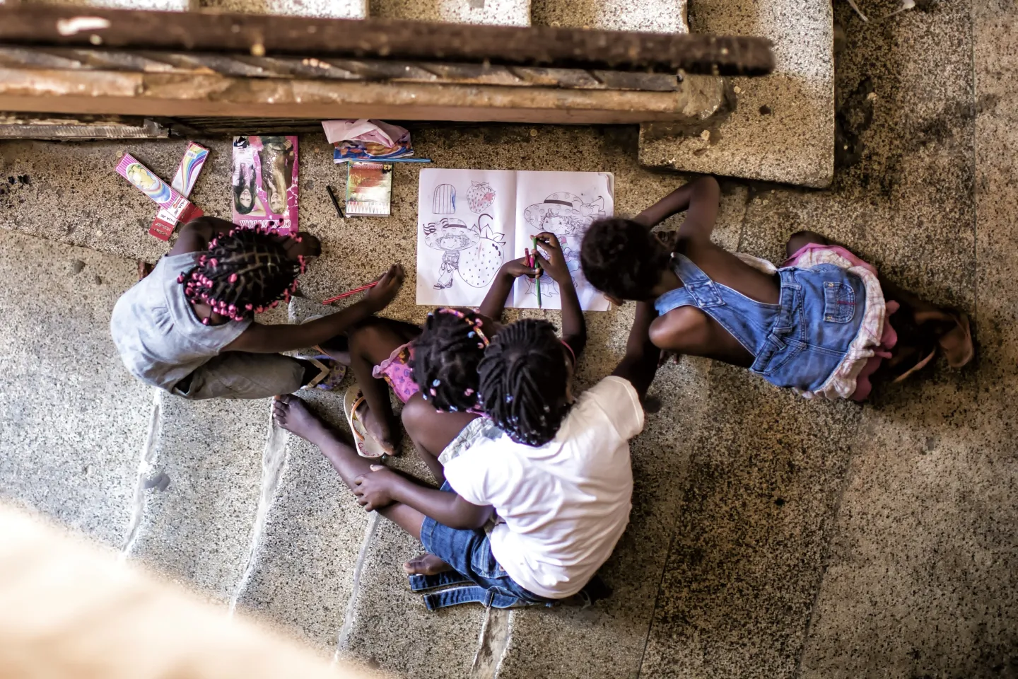 Crian&ccedil;as fazem desenhos e pintam sentados no ch&atilde;o na entrada de um pr&eacute;dio