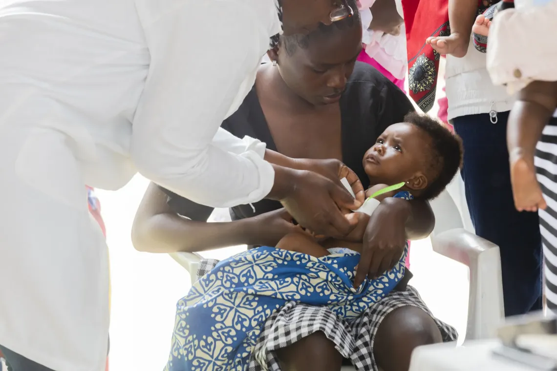 Em Ba&iacute;a Farta, prov&iacute;ncia de Benguela, Ana segura com cuidado a sua filha enquanto uma agente comunit&aacute;ria de sa&uacute;de mede o bra&ccedil;o pequeno da crian&ccedil;a com uma fita simples e colorida.