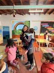 En un aula la maestra sube a una ni&ntilde;a en sus espaldas y sonrie