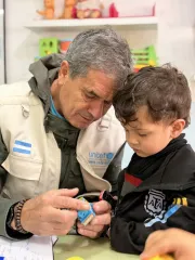 Personal de UNICEF con chaleco y ni&ntilde;o con abrigo negro jugando juntos con un trencito