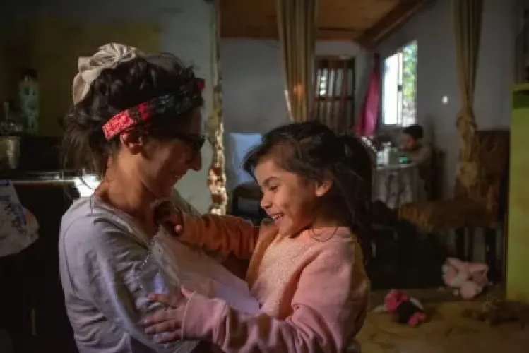 Mujer sosteniendo a su hija en brazos, ambas se miran y sonrien