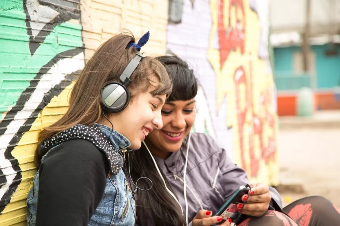 Dos adolescentes escuchando m&uacute;sica con sus celulares