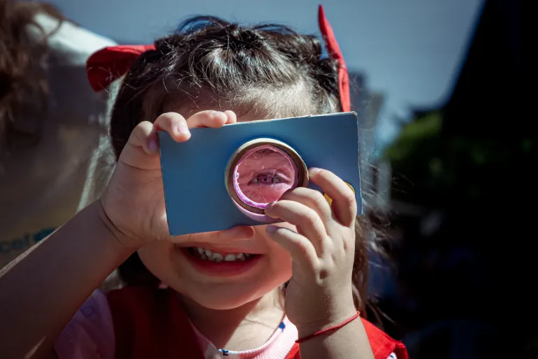 Una ni&ntilde;a sonriendo mir&aacute; atrav&eacute;s de una forma de carton color azul