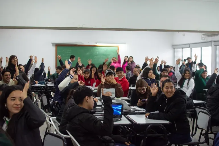 Un grupo de estudiantes en un aula alzan las manos