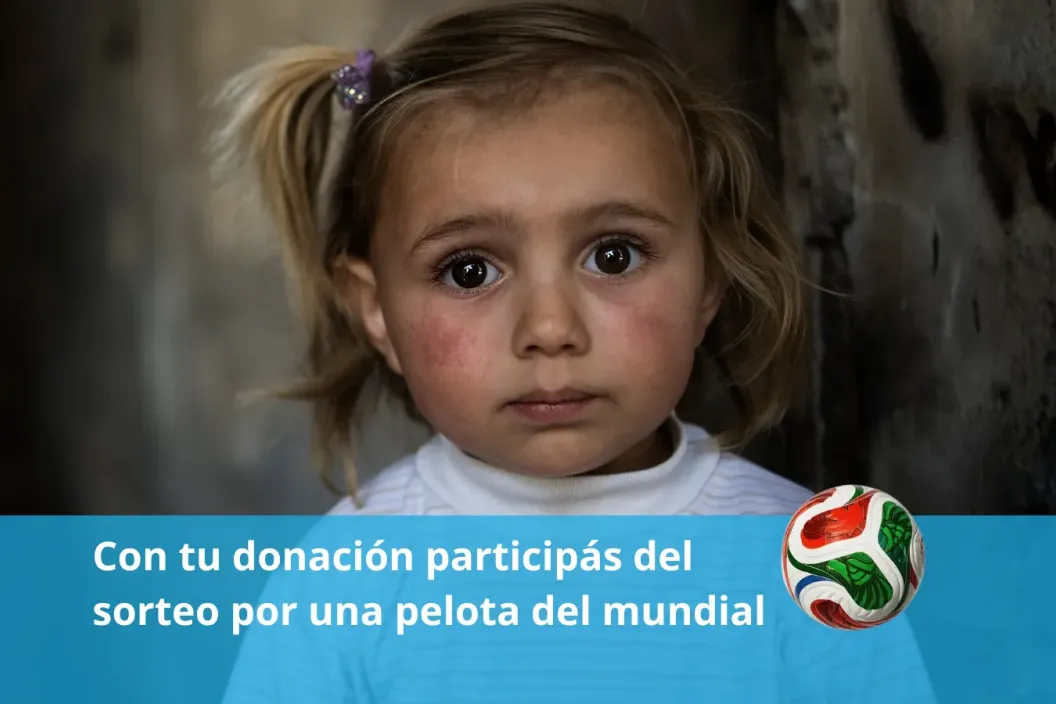 Una ni&ntilde;a en un barrio vulnerable mira a c&aacute;mara sosteniendo una pelota de f&uacute;tbol.
